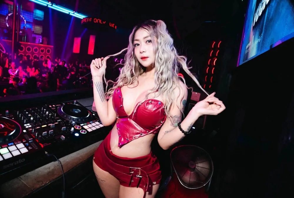 DJ VOCKA in a dark club booth, the floor lit behind her